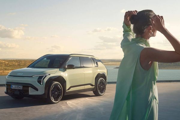Ein parkender Kia Ev3 vor einem See und im Vordergrund steht eine Frau